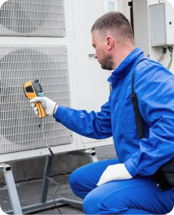 An HVAC technician in a blue jumpsuit using a thermal imaging camera to perform advanced diagnostics on a commercial outdoor AC unit.