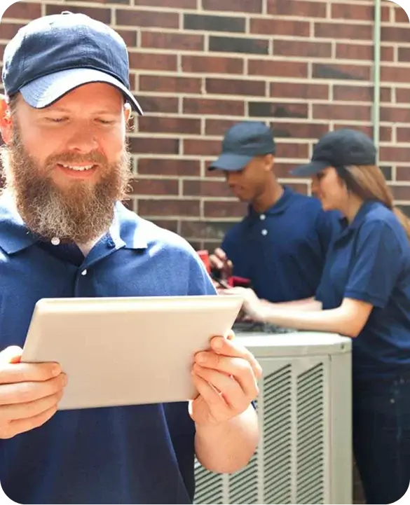 A lead HVAC technician reviews results on a tablet while two team members work on an outdoor AC unit in the background.