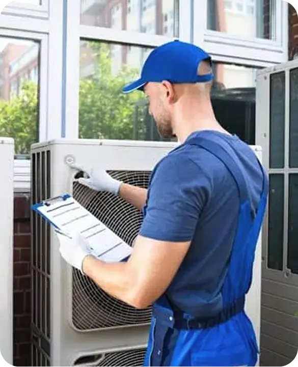 An HVAC technician in a blue uniform inspecting an outdoor air conditioning unit with a clipboard during a routine maintenance check.