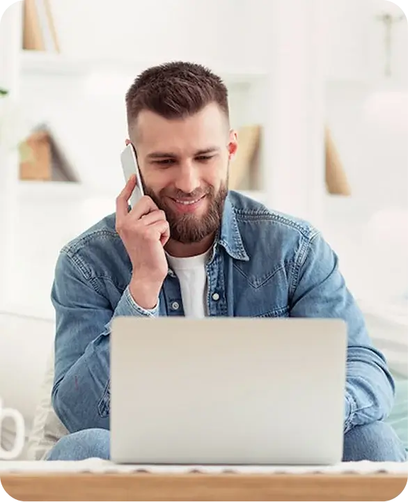 Smiling man on phone call beside open laptop at home