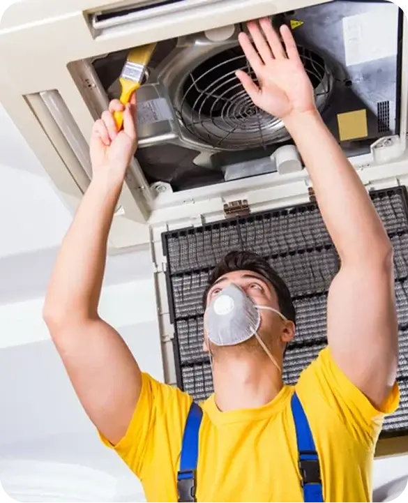 HVAC technician wearing a respirator mask cleaning and repairing a ceiling-mounted residential air conditioning unit