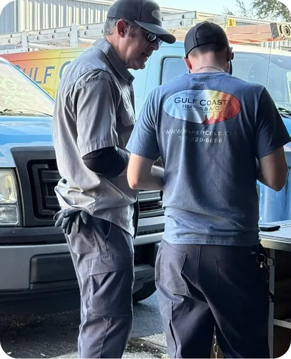 Two Gulf Coast Heating and AC technicians reviewing job details next to a branded service truck before an HVAC service call