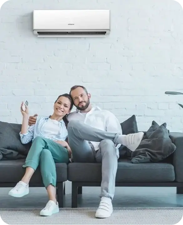 Happy couple relaxing on a couch at home with a wall-mounted mini split air conditioner, enjoying Gulf Coast Heating and AC comfort