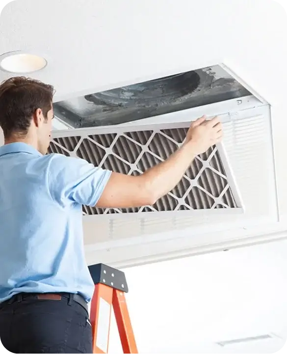Technician replacing dirty air duct filter on ladder